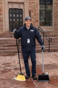CCS Employee outside of an education facility holding a broom and dust pan