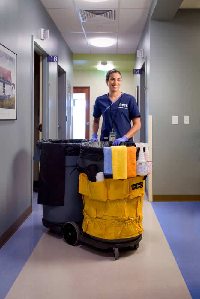 CCS Employee in a hallway with trash can and cleaning supplies